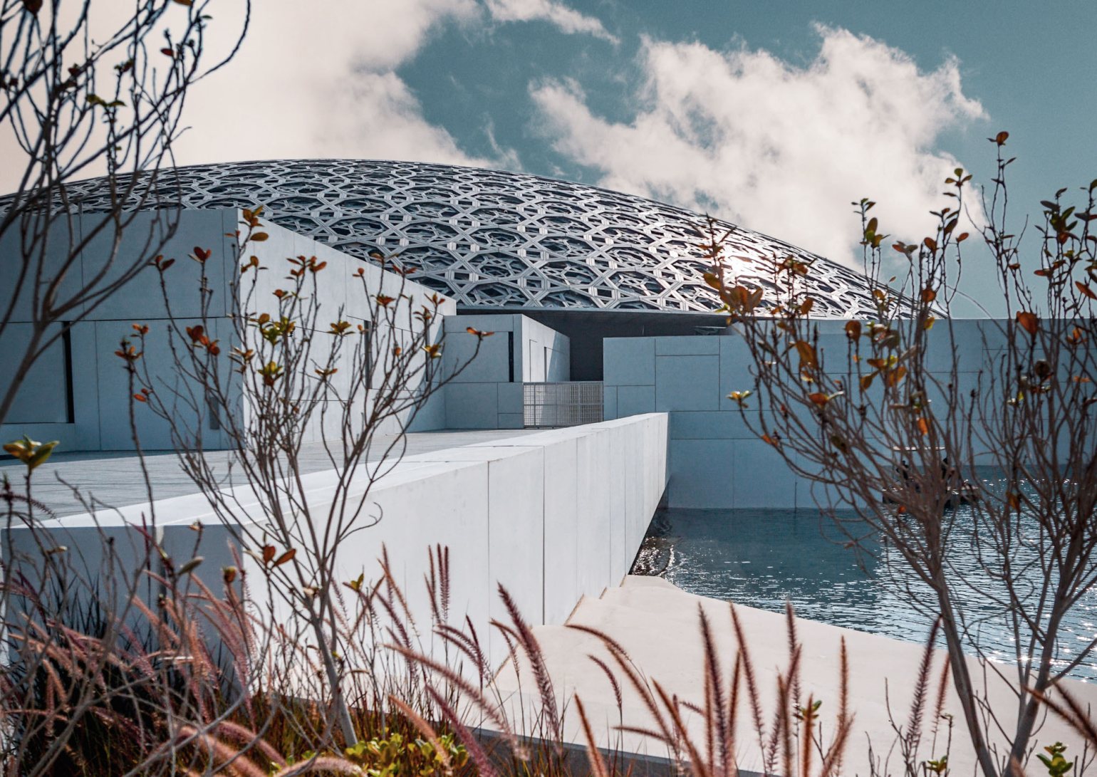 Exterior shot of Louvre Abu Dhabi, highlighting the silvery dome roof and concrete block architecture. Exterior shot of Louvre Abu Dhabi, highlighting the silvery dome roof and concrete block architecture.