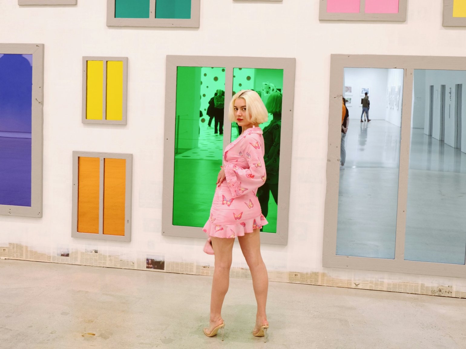 A person posing in front of a museum exhibition, with brightly coloured reflected panels.