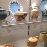 Enclosed museum display featuring various crockery and teapots with correlating information on shelf edge label holders.