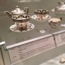 Enclosed museum display with hand-painted crockery and correlating information featured on shelf edge label holders.