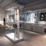 Museum exhibition with enclosed glass displays, featuring painted portraits, antiques and shelf edge label holders displaying