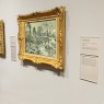 An artwork mounted in a golden frame and correlating information in label holders next to it.