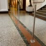 Four stainless steel Surface Mounted Q Barriers lined up horizontally facing the bottom of a staircase in a museum.